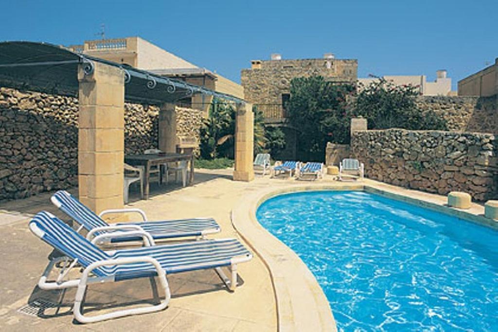 - une piscine avec des chaises longues et une table dans l'établissement "Steves Villas" Villa ta Rosi, à Ix-Xagħra