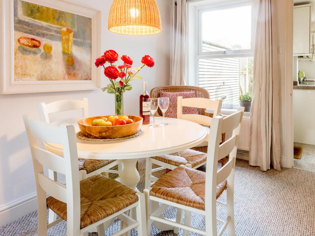 a white dining room with a white table with red roses at Walnut Cottage in Aldeburgh
