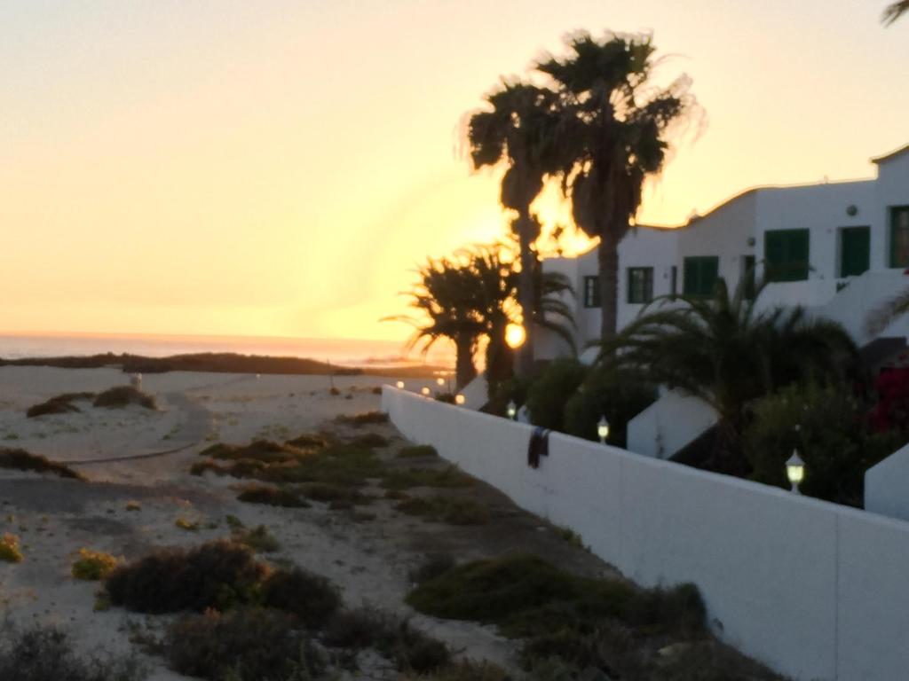 a sunset on the beach with palm trees and buildings at Cotillo Lagoons Apartment in Cotillo
