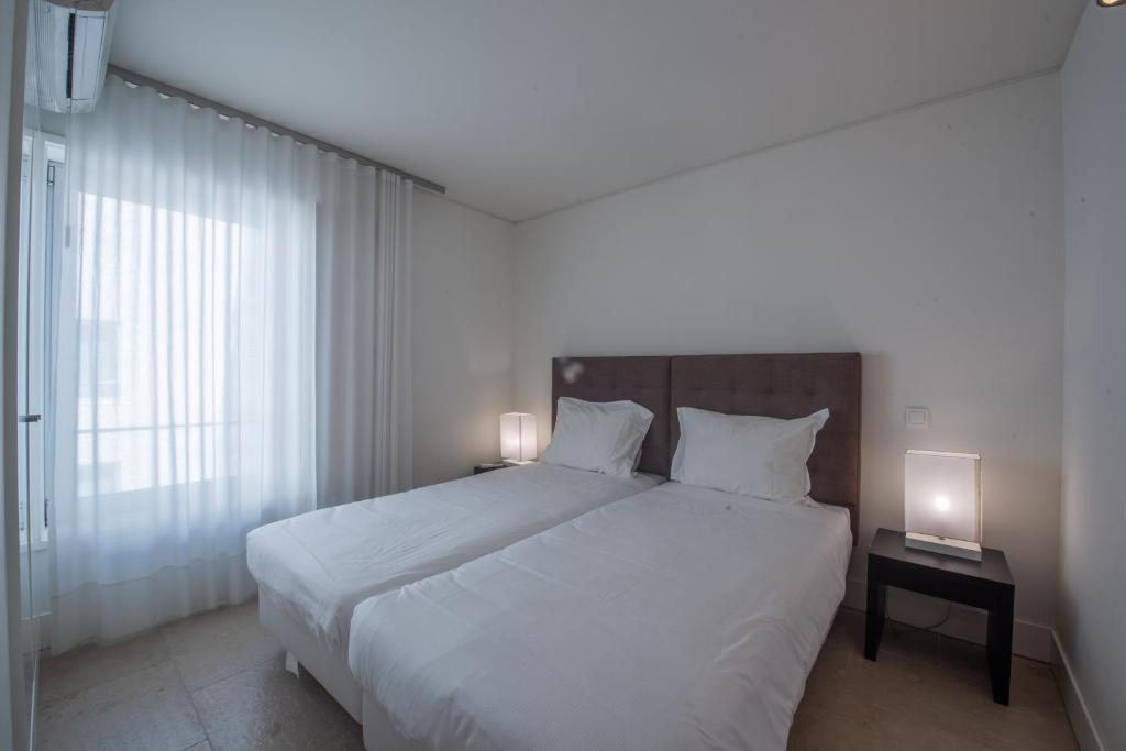 a bedroom with a large white bed with two lamps at Troia Residence by The Editory - Apartamentos Marina in Troia