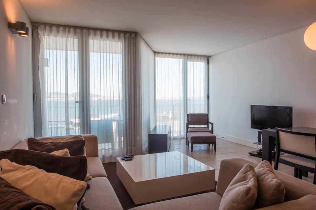 a living room with a couch and a tv and some windows at Troia Residence by The Editory - Apartamentos Marina in Troia