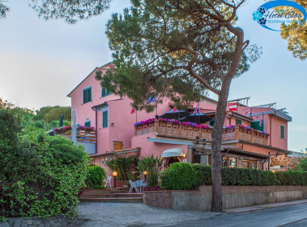 una casa rosa con un albero di fronte di Hotel Elba a Marina di Campo