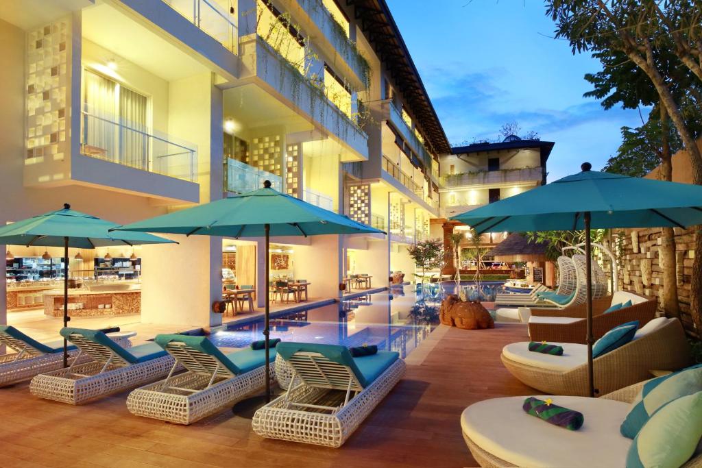 a patio with chairs and umbrellas and a pool at Jimbaran Bay Beach Resort and Spa by Prabhu in Jimbaran