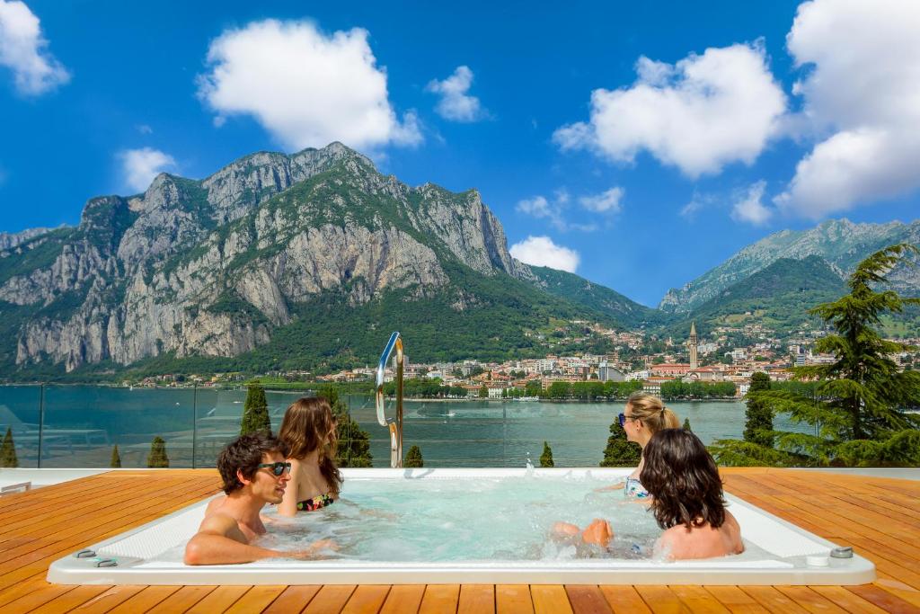 a group of people sitting in a hot tub with mountains at Hotel Griso Collection in Malgrate