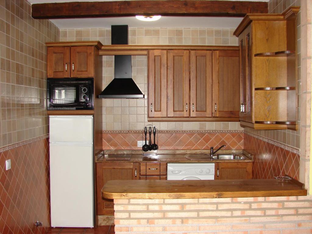 Una cocina con gabinetes de madera y un refrigerador blanco. en Apartamentos Sierra de Segura, en Segura de la Sierra