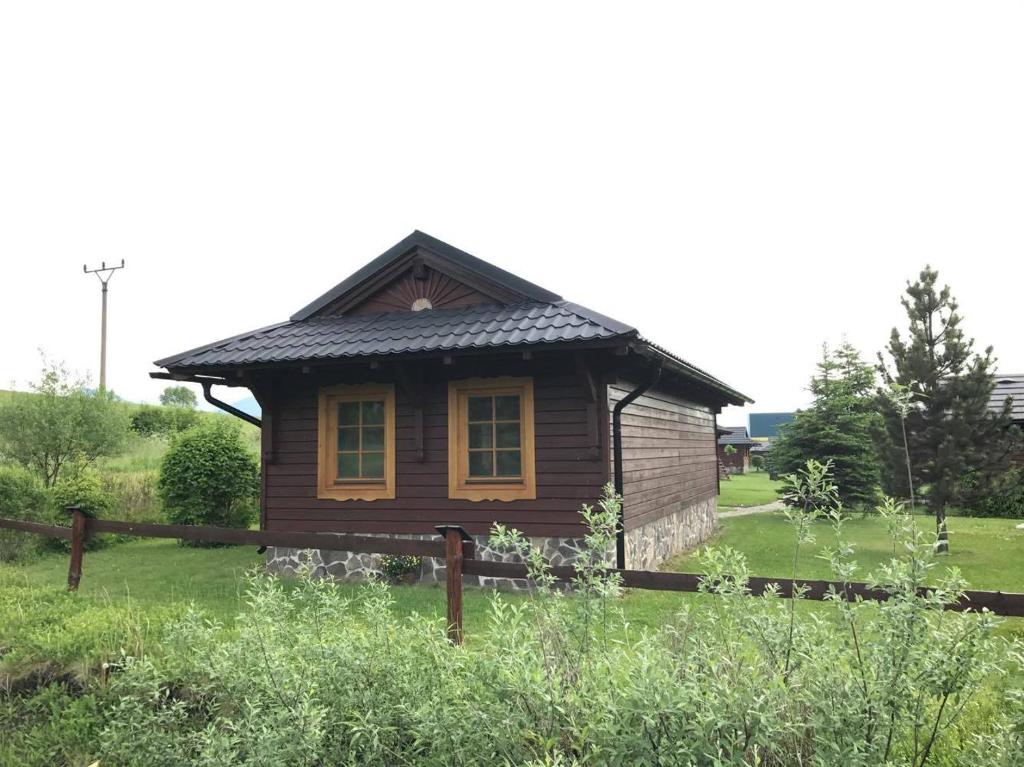 a small wooden house in a field with a fence at Chatka Tatralandia 114 in Liptovská Ondrašová