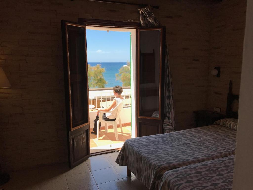 a woman sitting on a chair on a balcony looking at the ocean at Hostal Restaurante Playa in Colònia de Sant Jordi