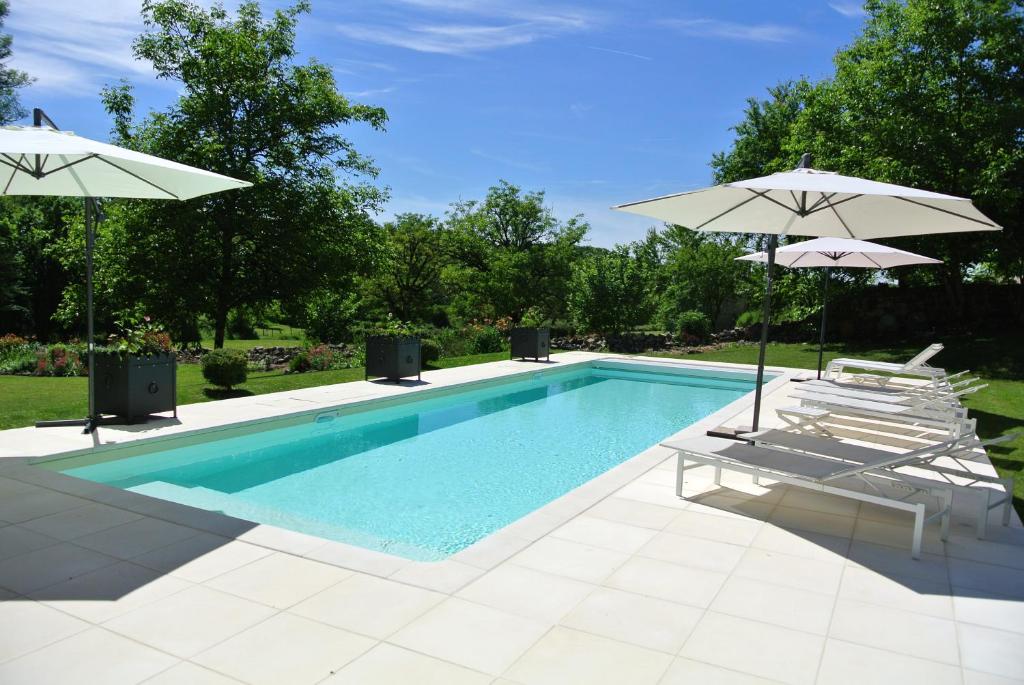 a swimming pool with two umbrellas and two chairs and a swimming pool at Chambre d&#39;hôtes Au jardin de la Bachellerie in La Bachellerie