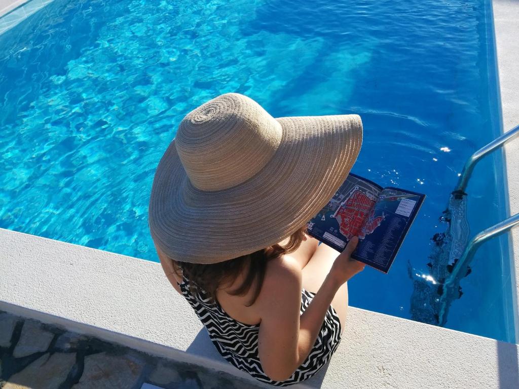 a woman wearing a hat reading a book next to a pool at Apartments Anamaria in Dubrovnik