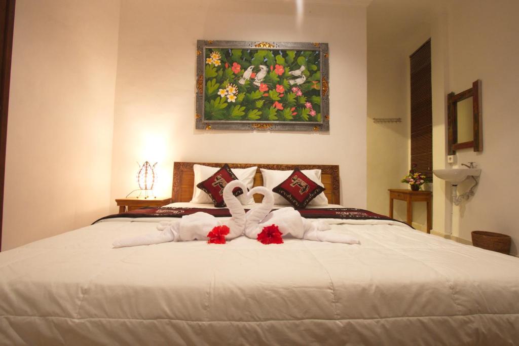 - une chambre avec un lit, des serviettes blanches et des fleurs rouges dans l'établissement Uma Loris Ubud, à Ubud