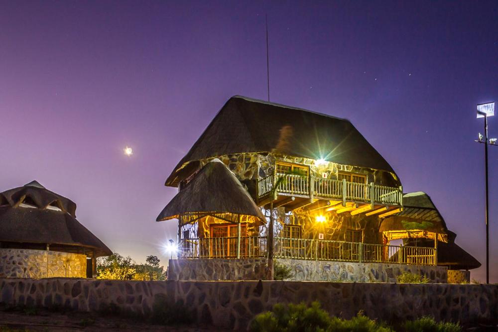 a building with a thatched roof at night at Big Valley Game Lodge in Lobatse