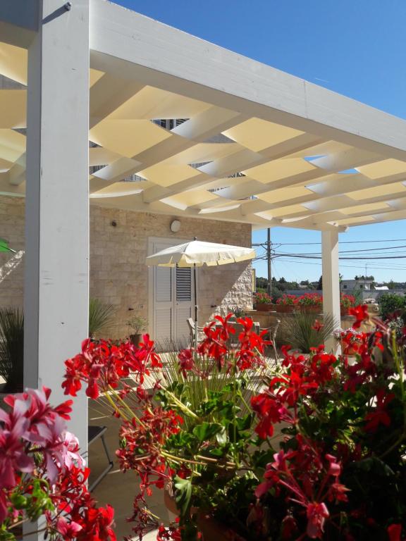 a patio with red flowers and an umbrella at B&b Gaestehaus Tagaro in Locorotondo