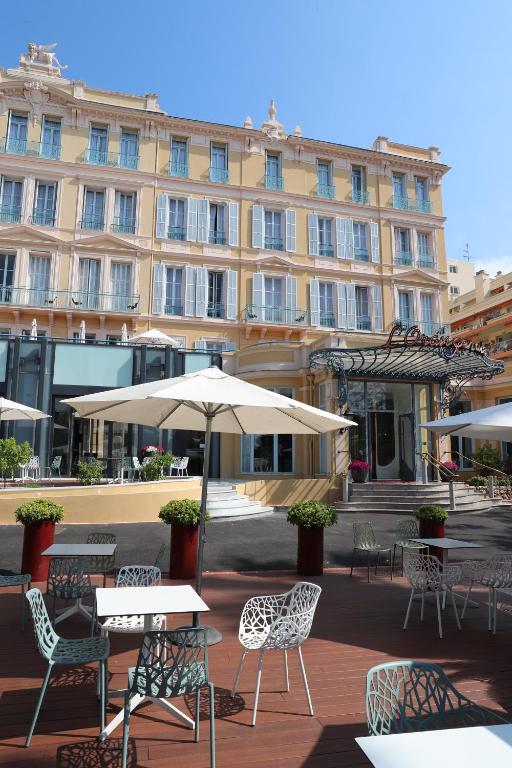 a building with tables and chairs and an umbrella at Hôtel Miléade L'Orangeraie - Menton in Menton