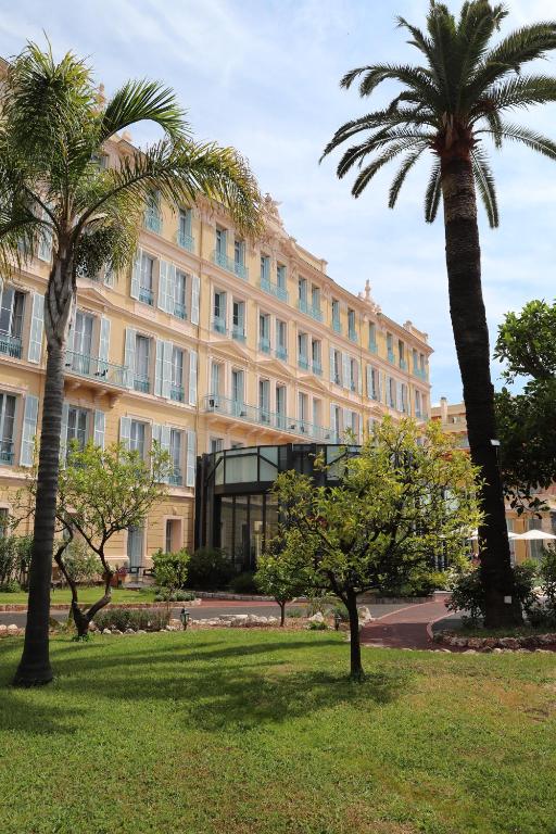 a large building with palm trees in a park at Hôtel Miléade L'Orangeraie - Menton in Menton