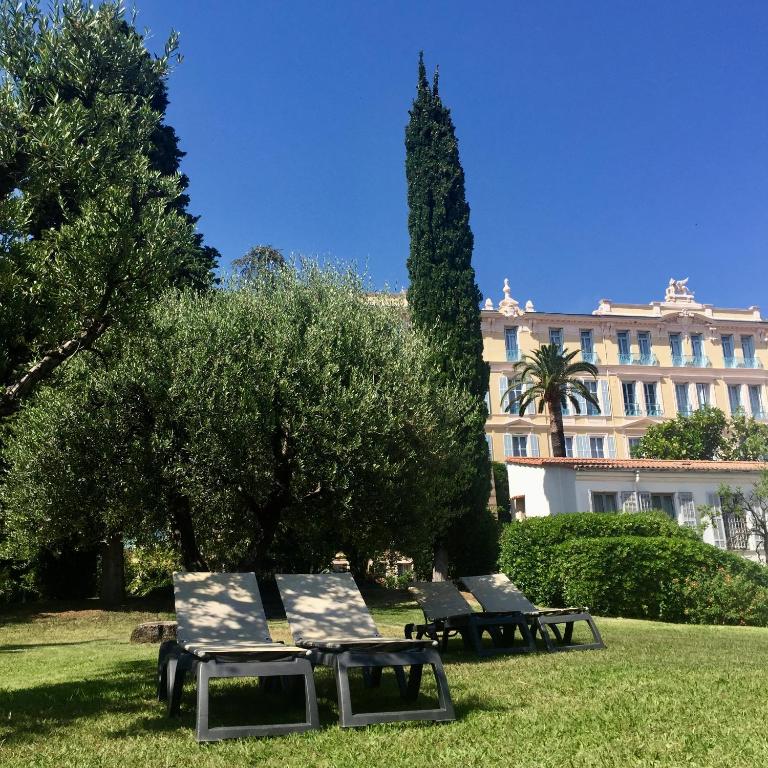 two benches in a park in front of a building at Hôtel Miléade L'Orangeraie - Menton in Menton