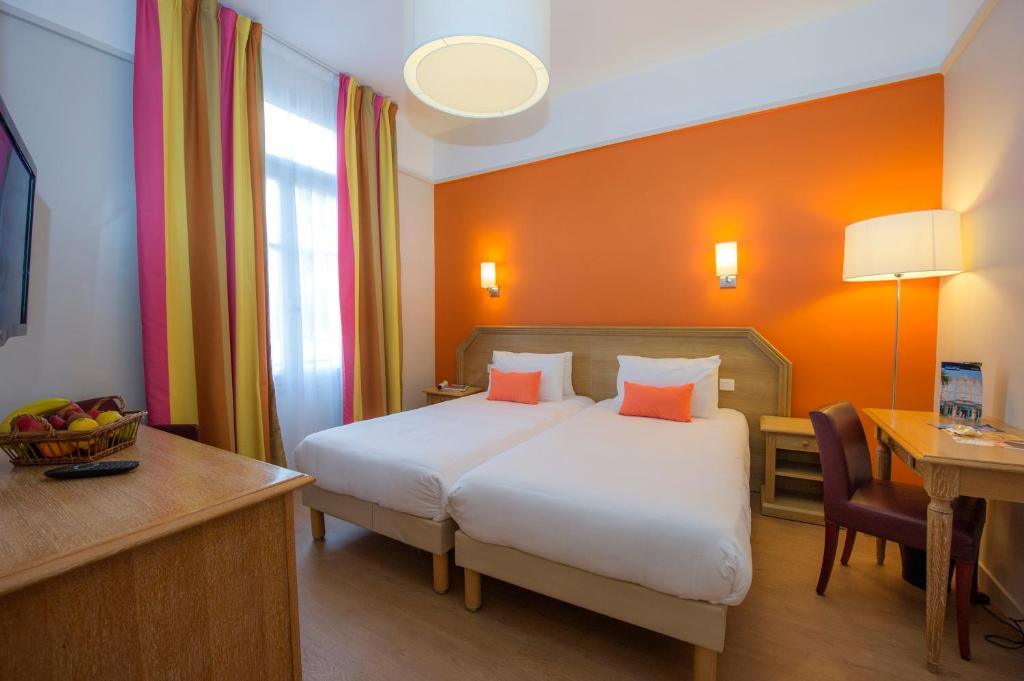 a hotel room with a bed and a desk and a table at Hôtel Miléade L'Orangeraie - Menton in Menton