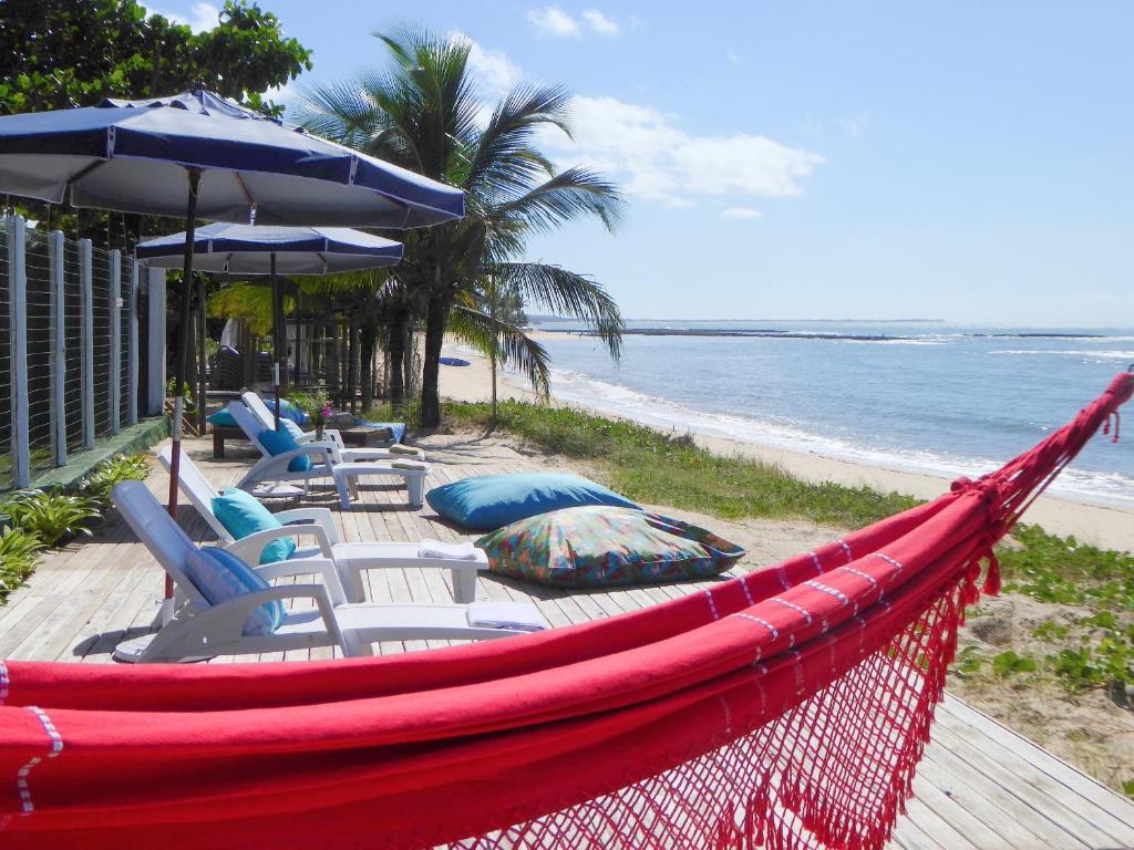 a hammock with chairs and umbrellas on a beach at Ouro Sobre Azul Apart Hotel in Arraial d'Ajuda