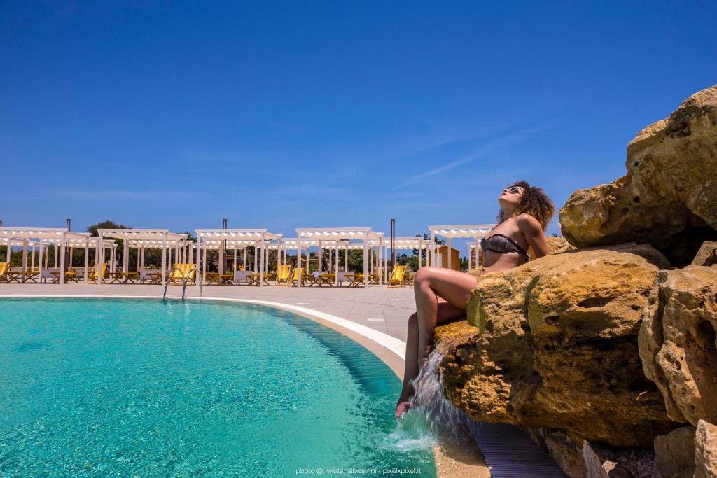 a woman sitting on a rock next to a swimming pool at Hotel Casale Milocca in Siracusa