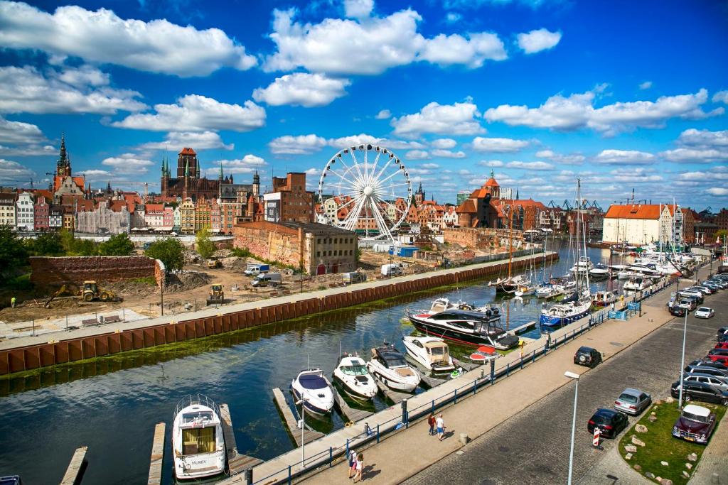 a city with boats docked in a river with a ferris wheel at Drim Apartaments in Gdańsk