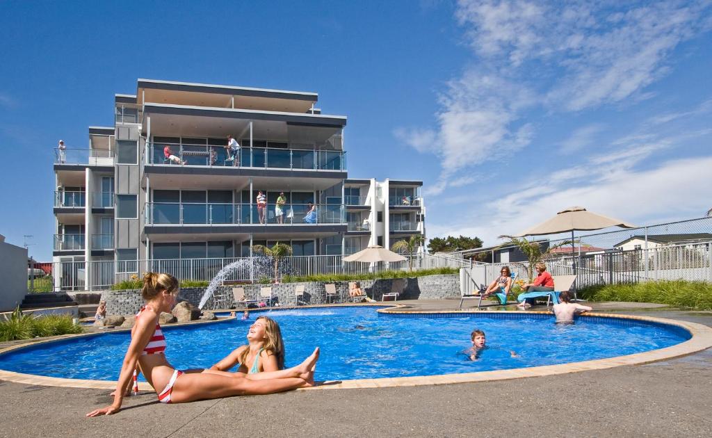 dos chicas sentadas en la piscina en un resort en Ohope Beach Resort en Ohope Beach