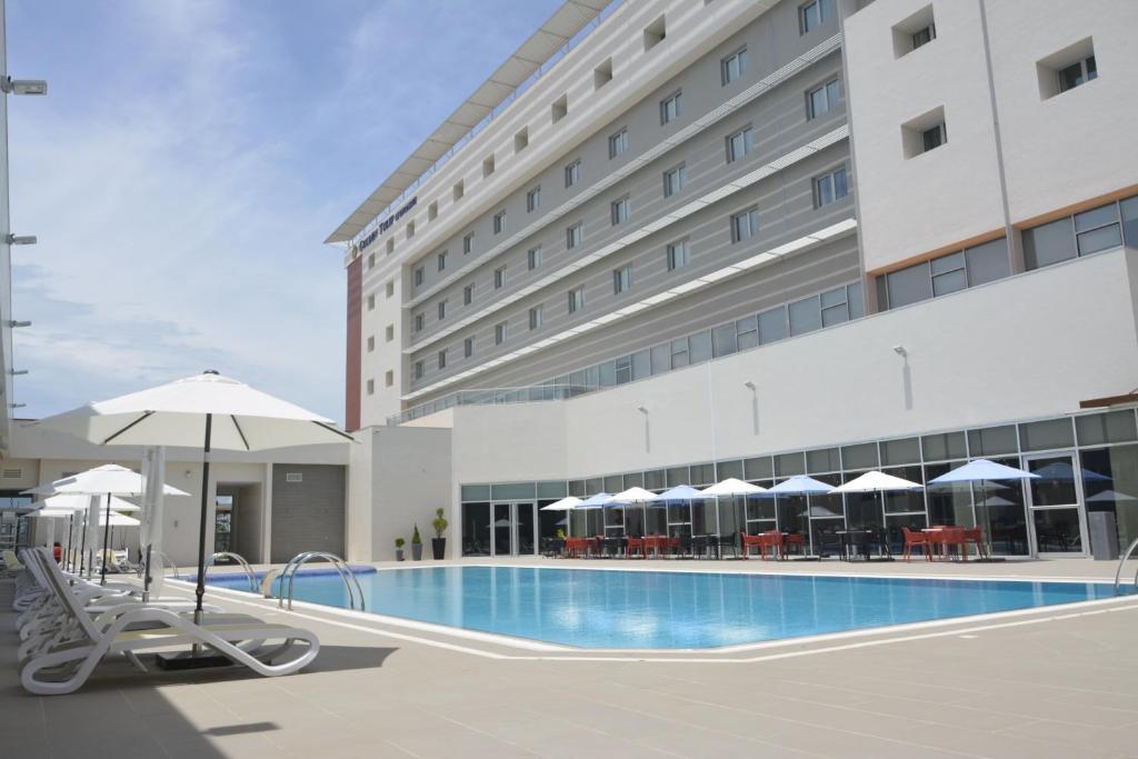 uma piscina do hotel com cadeiras e guarda-sóis em frente a um edifício em Golden Tulip Le Diplomate em Cotonou