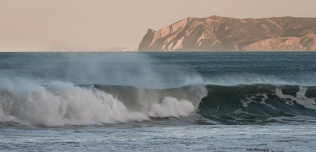 a large wave in the ocean with a mountain in the background at Ocean View Beachfront Apartment in Blenheim