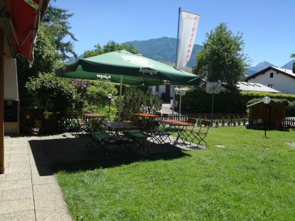 a picnic table with a green umbrella in the grass at Hotel-Restaurant Zum Hirschhaus in Ruhpolding