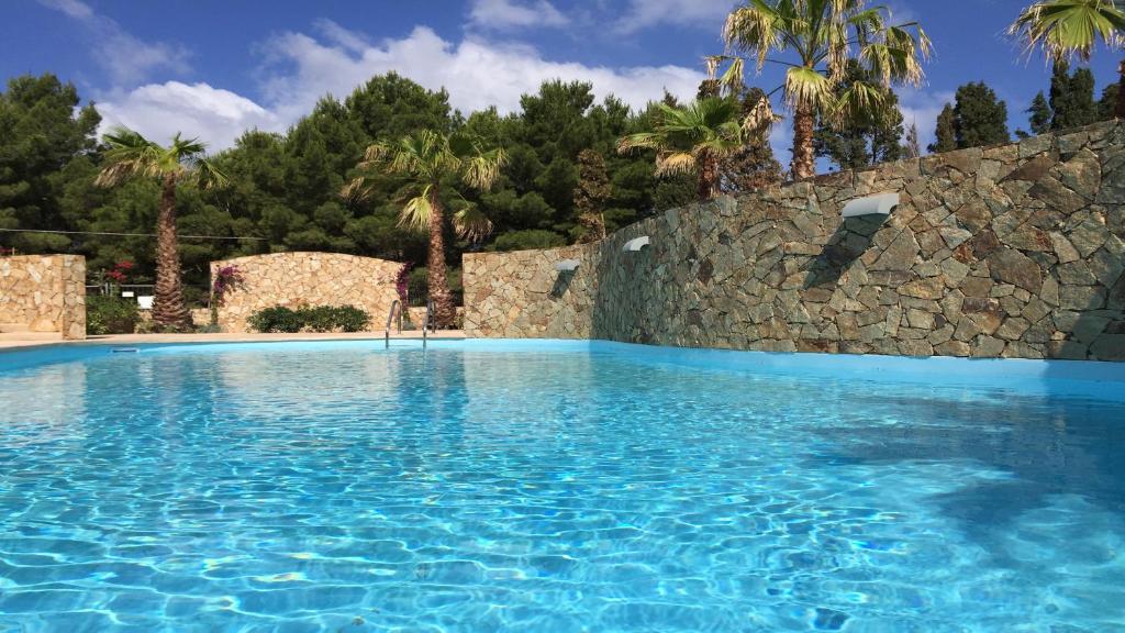 a swimming pool with blue water and a stone wall at Residence Elegance in Porto Pino