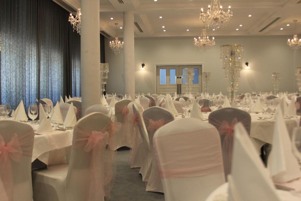 a banquet hall with white tables and chairs and chandeliers at Yarrow Hotel in Broadstairs