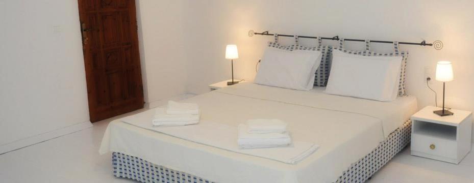 a white bedroom with a white bed with two lamps at Porto Elea Camping & Bungalows in Metókhion Zográfou