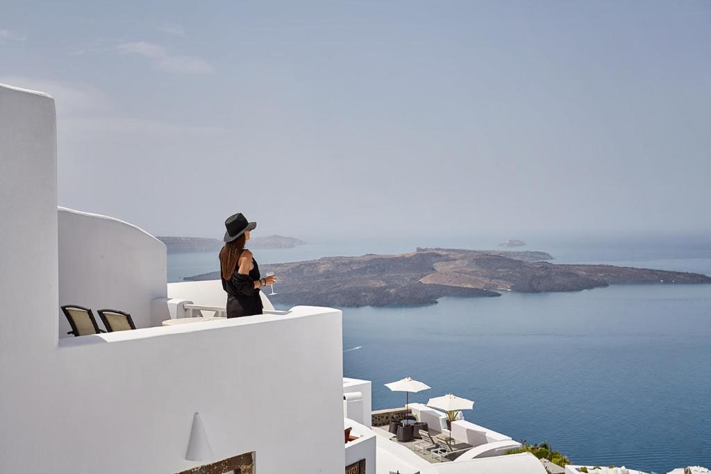 a woman sitting on the edge of a building looking at the ocean at Mirabo Villas in Firostefani