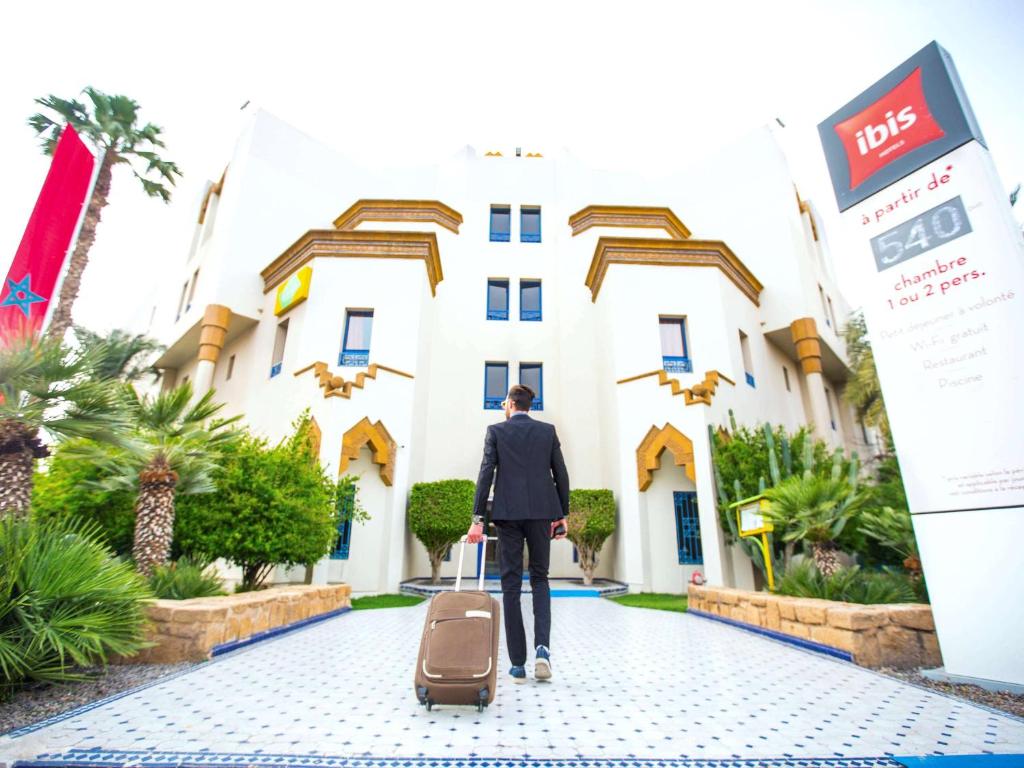 un hombre con una maleta caminando hacia un hotel en Ibis Oujda en Oujda