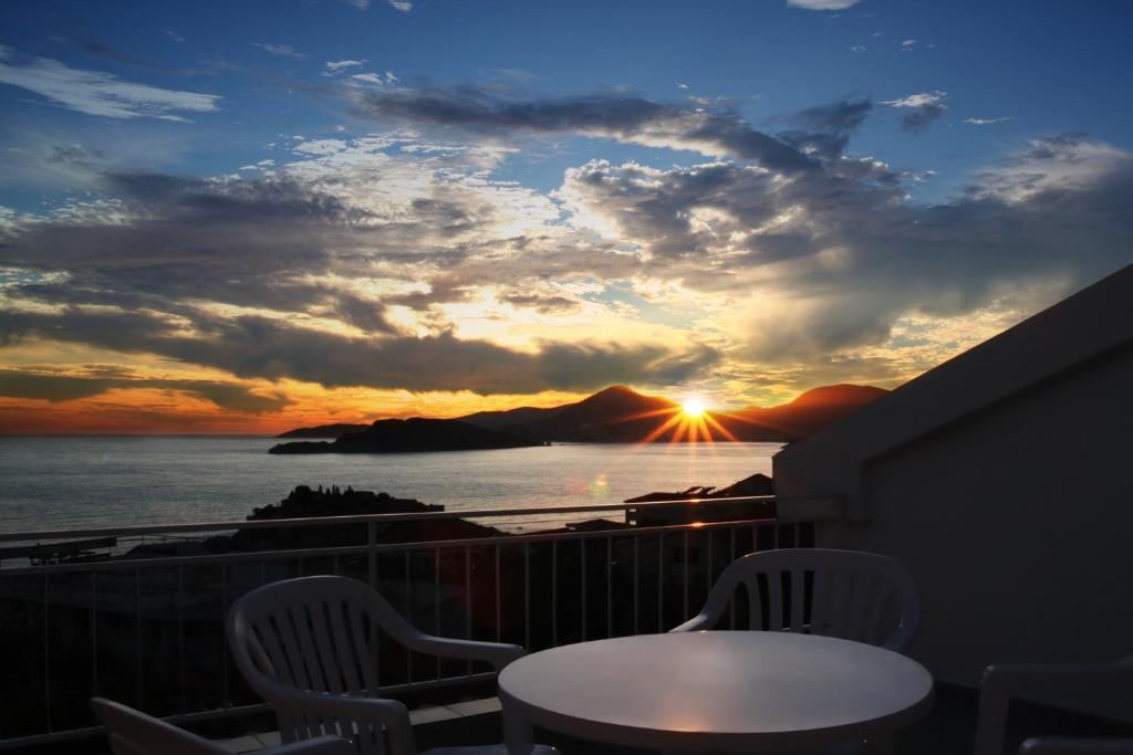 a sunset from a balcony with a table and chairs at Apartments Antonela in Sveti Stefan