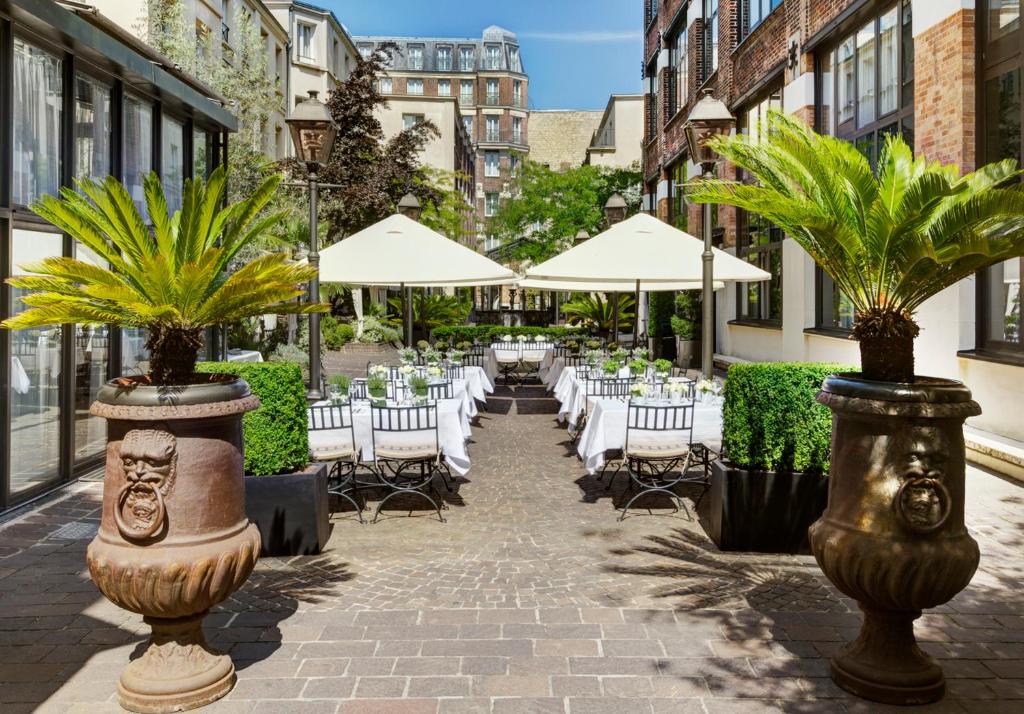 un patio con mesas, sillas y sombrillas en Les Jardins Du Marais, en París