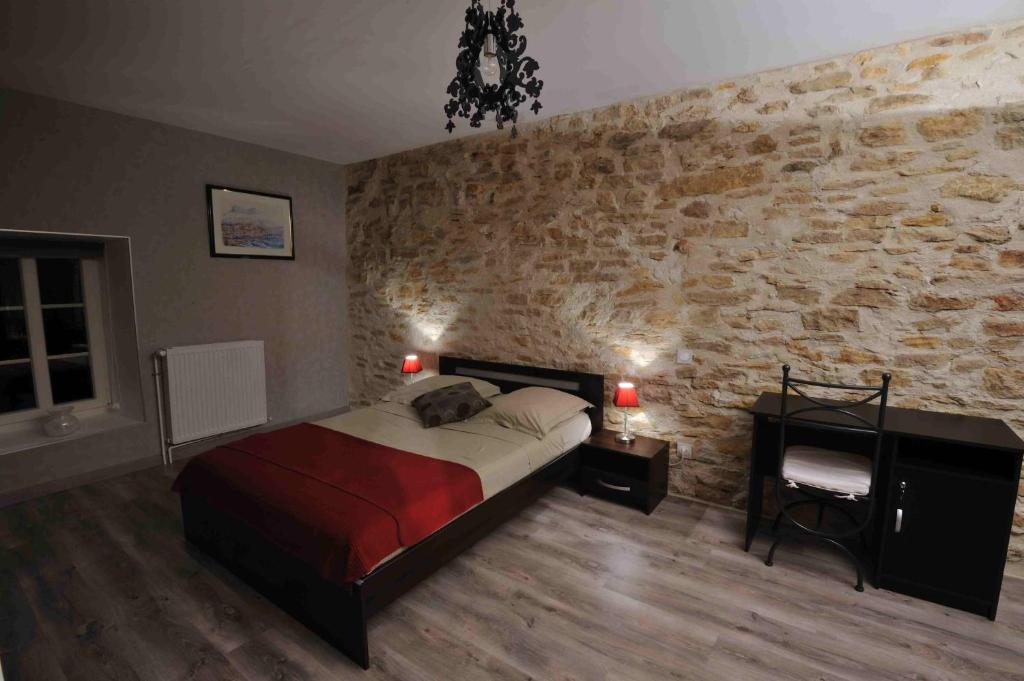 Les Chambres d'Eponine في Saints-Geosmes: غرفة نوم بسرير وجدار حجري