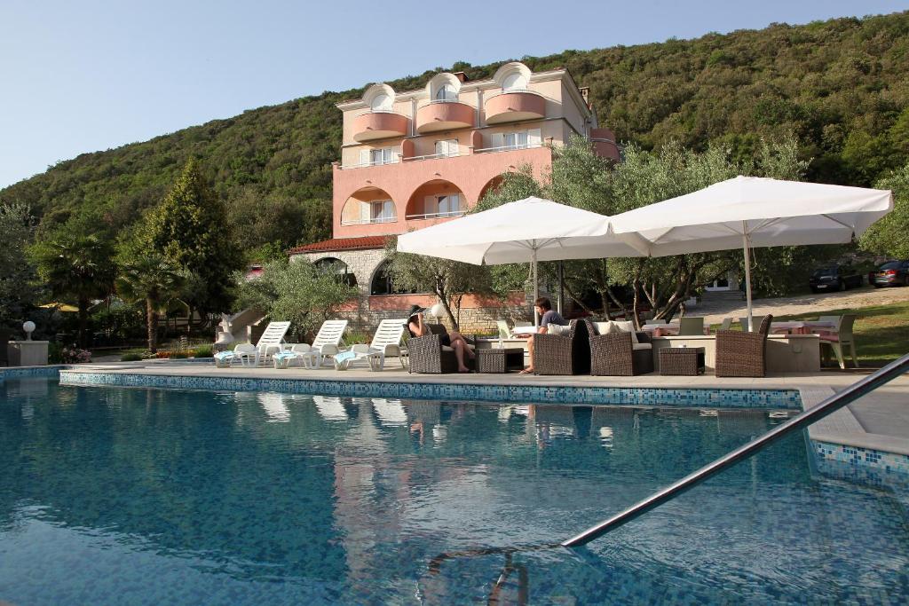 a pool with chairs and umbrellas next to a building at Hotel Carmen in Krnica