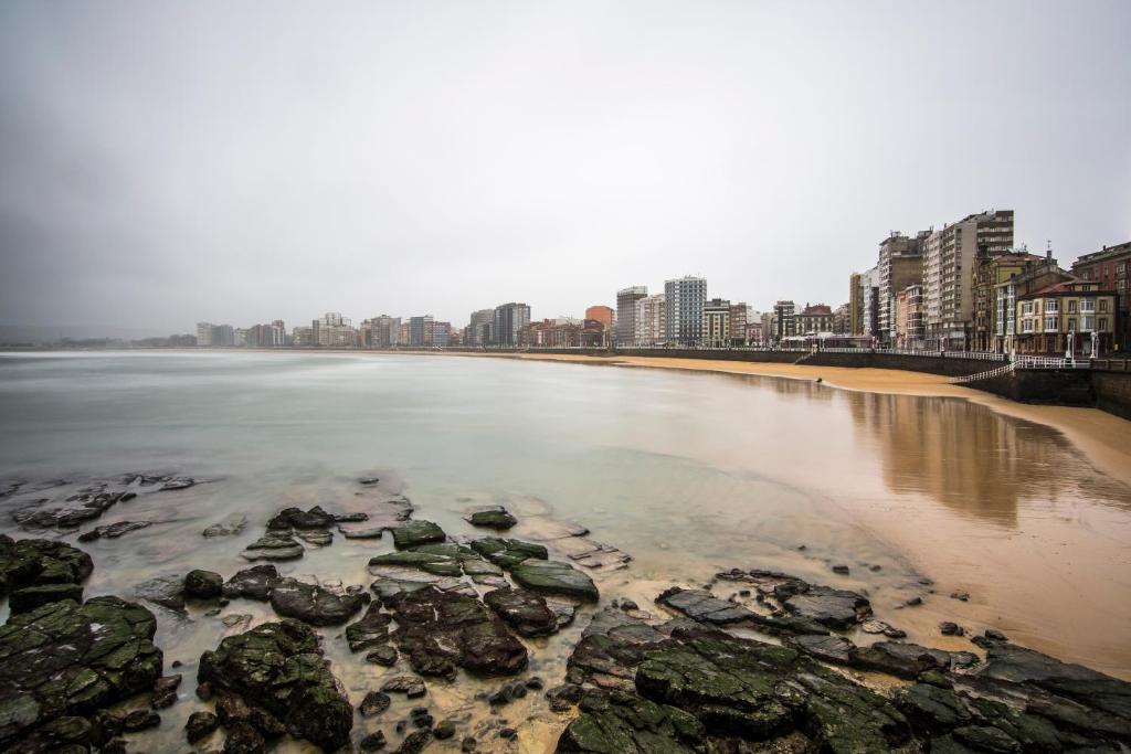 una playa con rocas en el agua y edificios en Hostal Libertad en Gijón