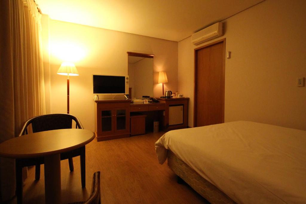 a hotel room with a bed and a desk and a table at Daedong Hotel in Jeju