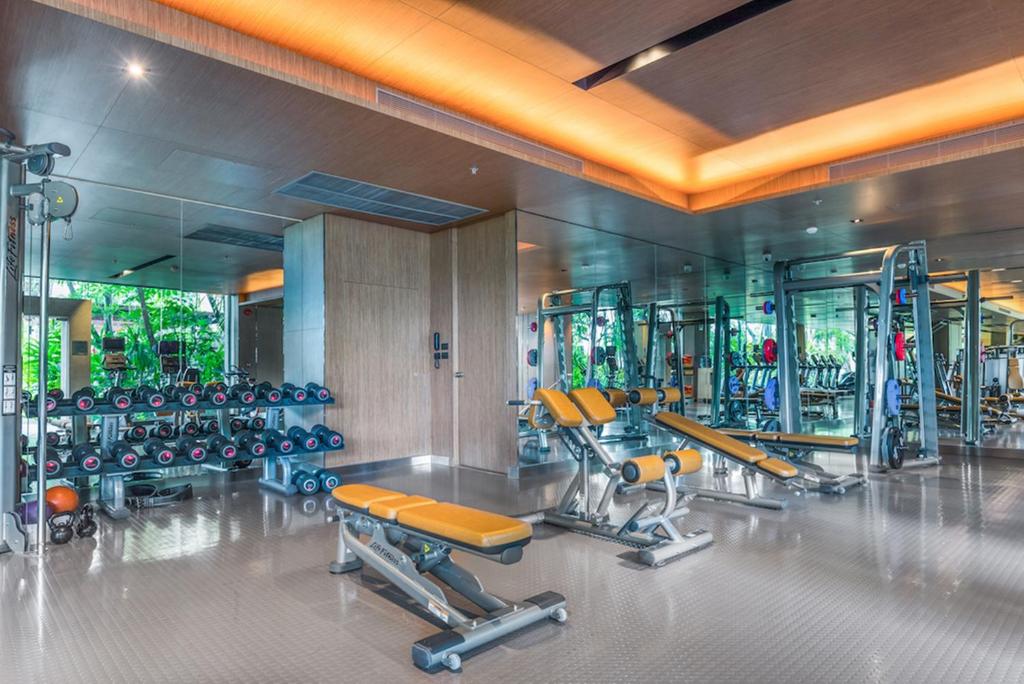 A bright, mirrored fitness room with strength equipment, dumbbells and benches.