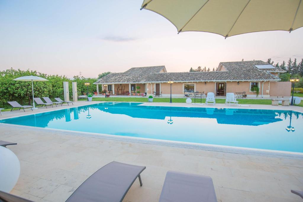 a large swimming pool with chairs and an umbrella at B&B Il Giardino di Sicilia in Case Monterosso