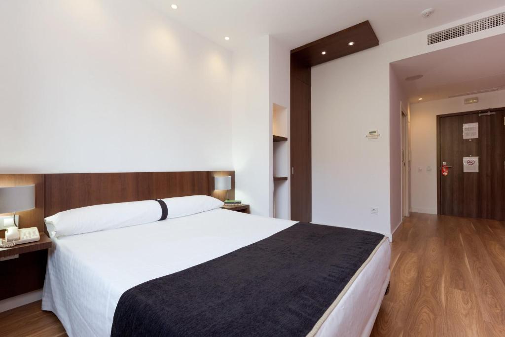 Hotel Olympia Universidades في فالنسيا: غرفة نوم بسرير ابيض كبير وارضية خشبية