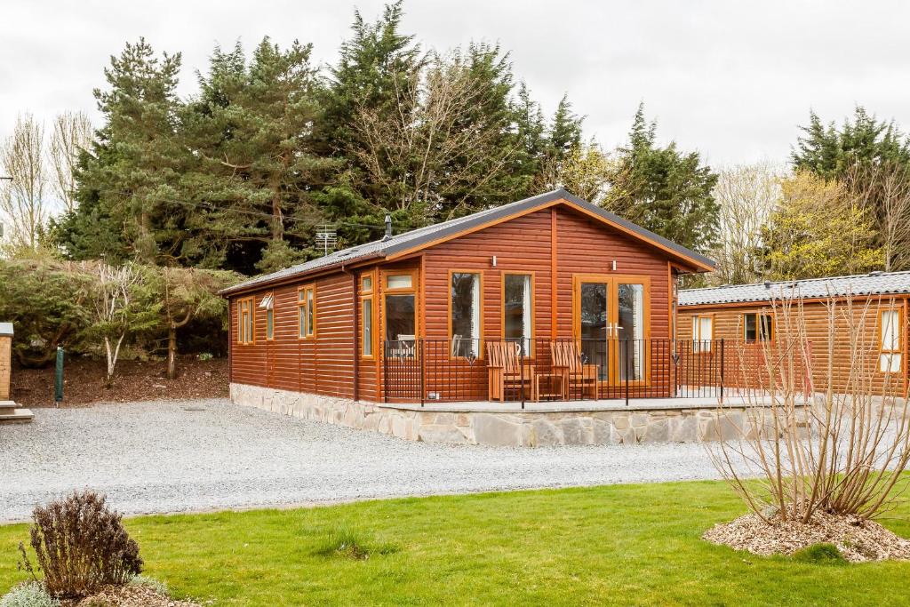 a wooden cabin with a porch in a yard at Thistle Lodge in Auchterarder