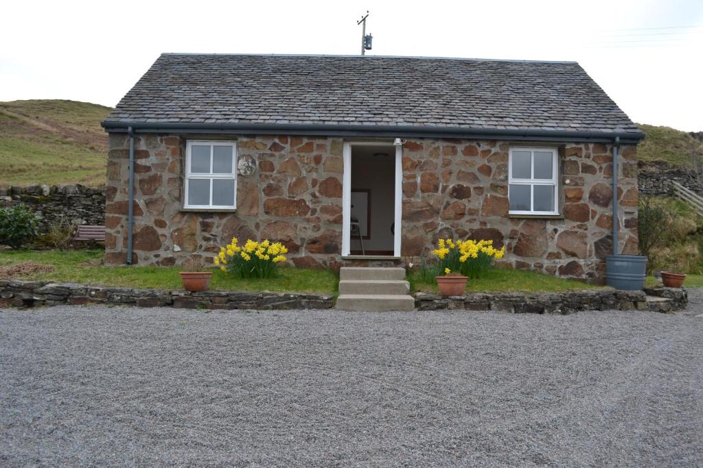 a stone house with yellow flowers in front of it at Oban Seil Farm The Bothy in Clachan