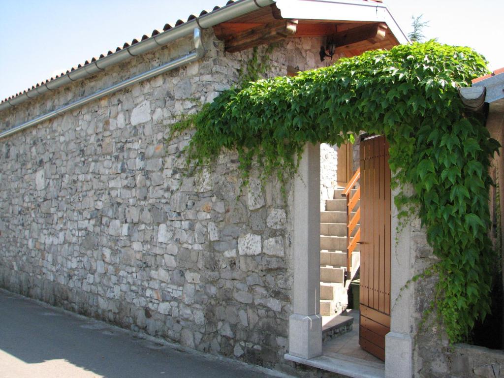 un edificio de piedra con una puerta de madera y un árbol en Apartma Furlan en Štanjel