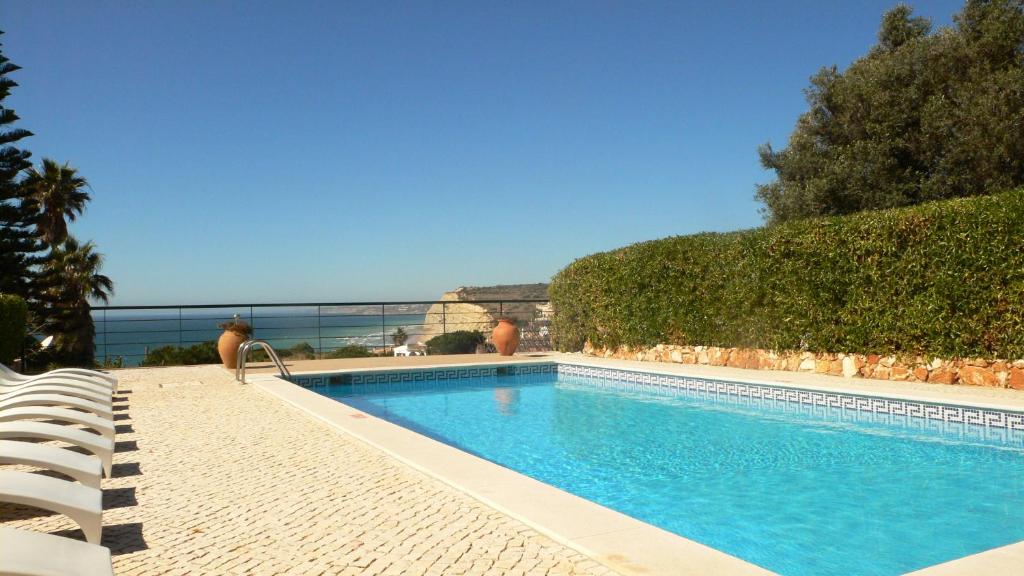 a swimming pool with chairs and the ocean in the background at Vivenda Solmar in Lagos