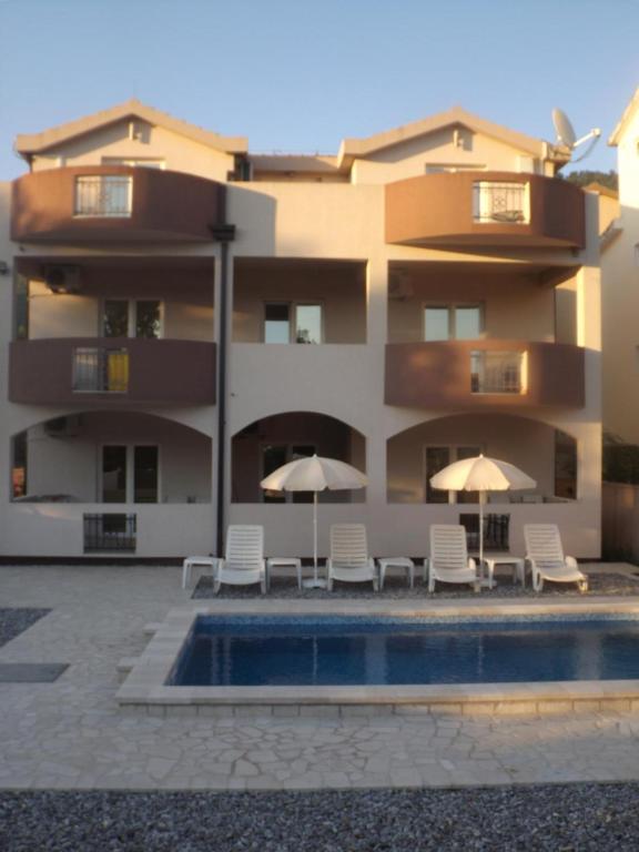 a building with chairs and umbrellas next to a swimming pool at Apartmani Bulajic in Tivat