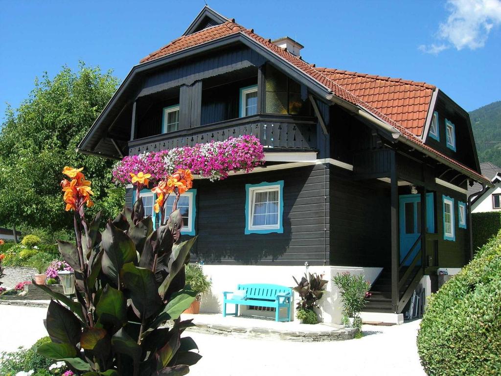 a black house with flowers and a blue bench at Haus Thon in Bodensdorf