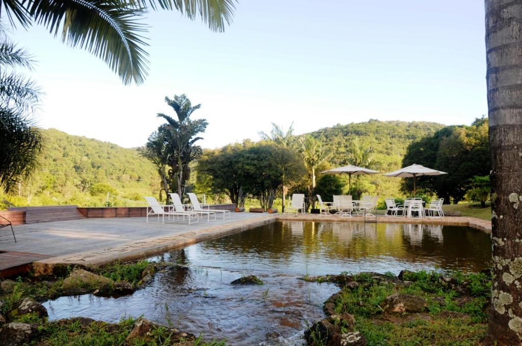 a pool with white chairs and tables and a lake at Hotel Fazenda Caco de Cuia in Itabirito