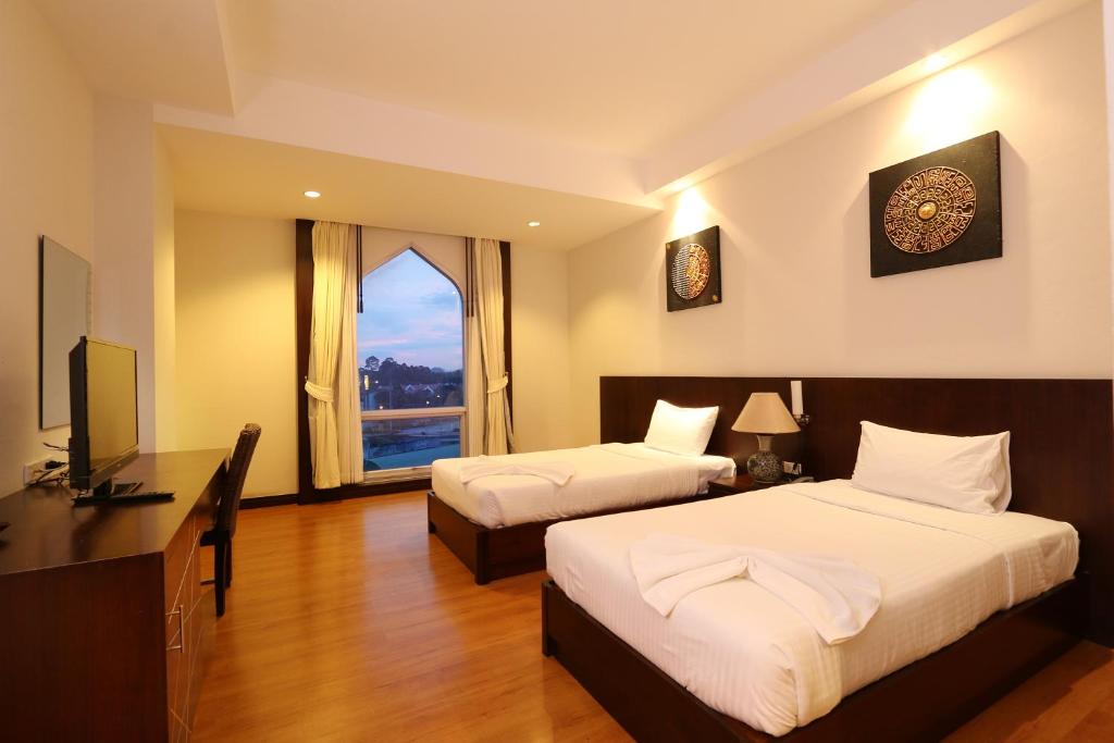 Habitación de hotel con 2 camas, escritorio y TV. en Grande Southern Hotel, en Thung Song