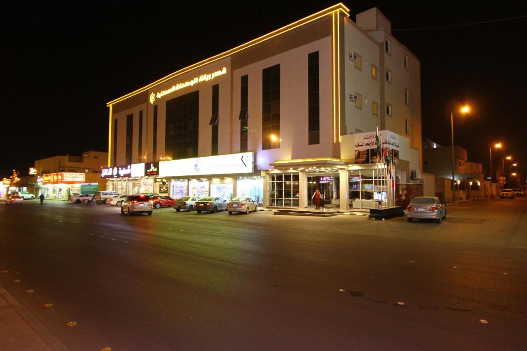 un edificio con coches estacionados en un estacionamiento por la noche en Qasr Rayana Aparthotel, en Buraidah
